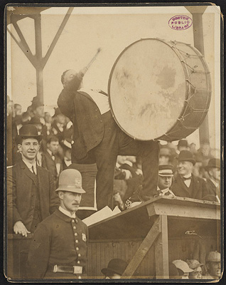 Photograph of Royal Rooter beating a drum, 1903 World Series. Photographer unidentified. Fan on the the visitors dugout provides percussion for the Boston American fans in game against the Pittsburgh Pirates. Boston Public Library McGreevey Collection. Accession No.: 06_06_000012