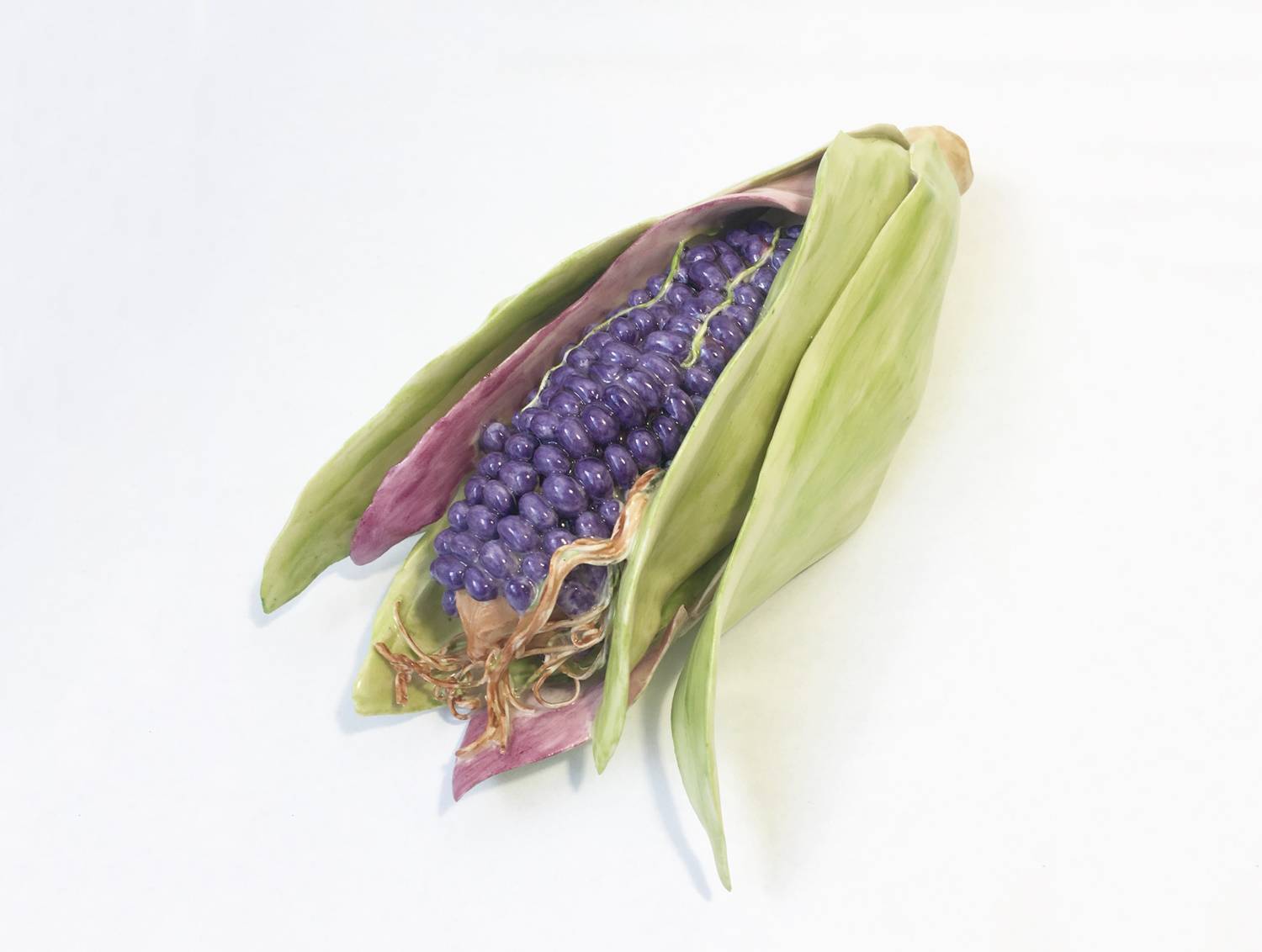 Ceramic sculpture of a purple corn cob with an open green husk.