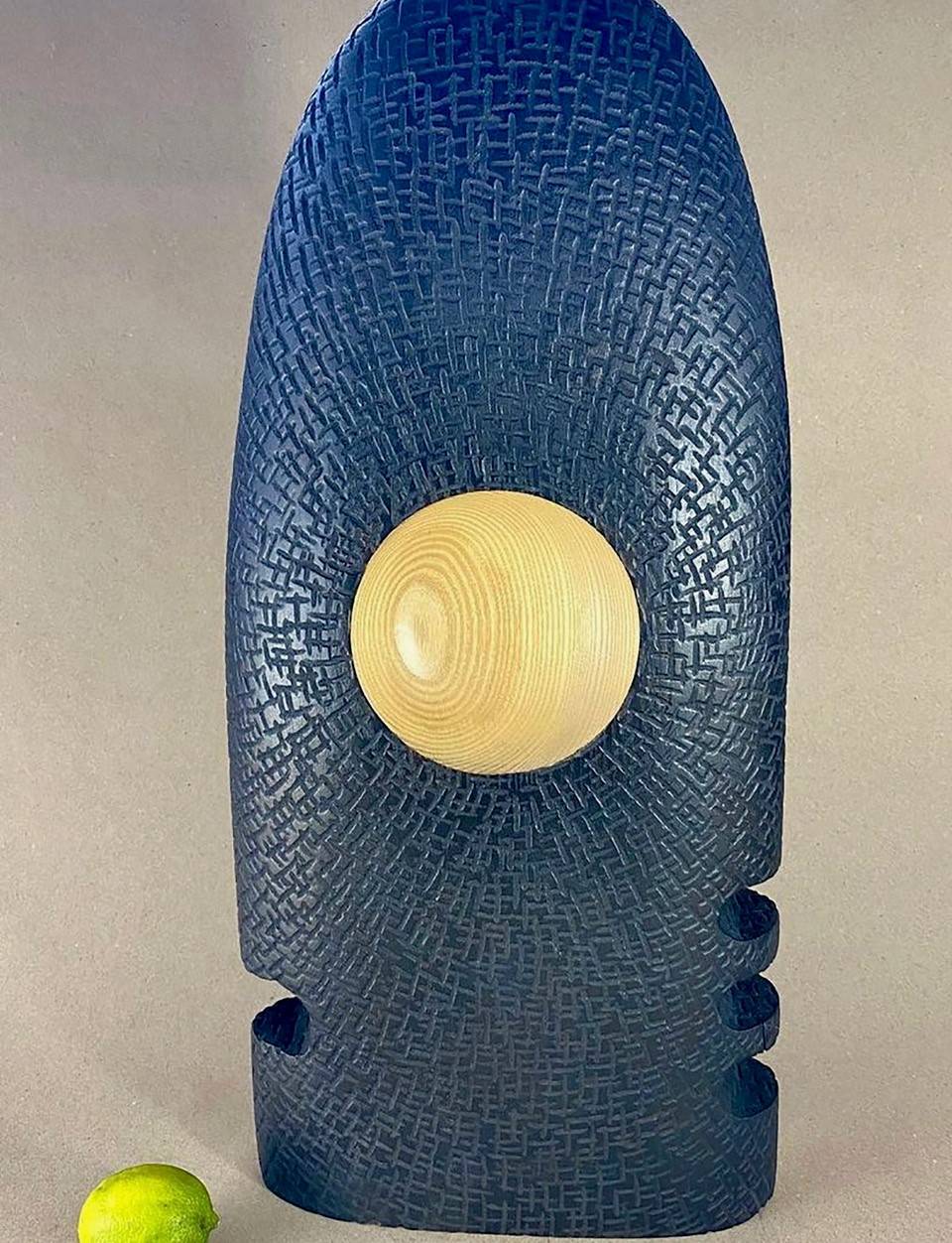 Abstract sculptural object resembling a blue rocket with a yellow circle in the center.