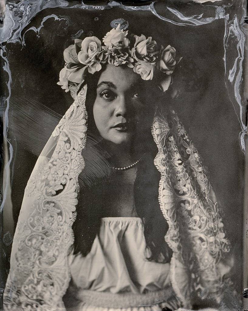 Photograph of a young bride with dark hair and a floral veil, made using tintype, a mid-1800s method of photography employing a thin sheet of metal.