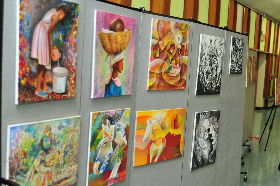 Wall lined with almost a dozen brightly colored paintings.