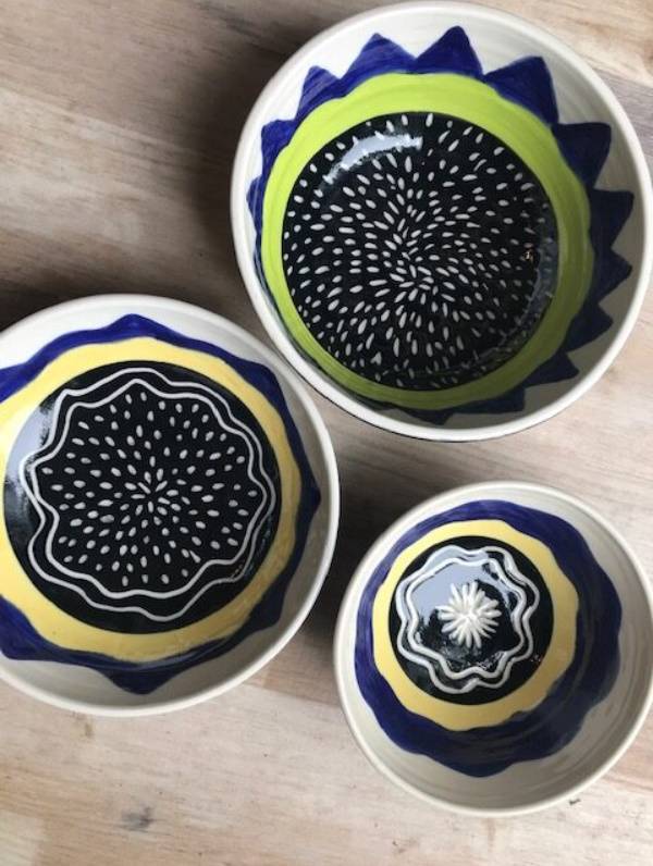 Three bowls seen from above with varied but similar black and white line and dot patterns and a yellow or green ring.
