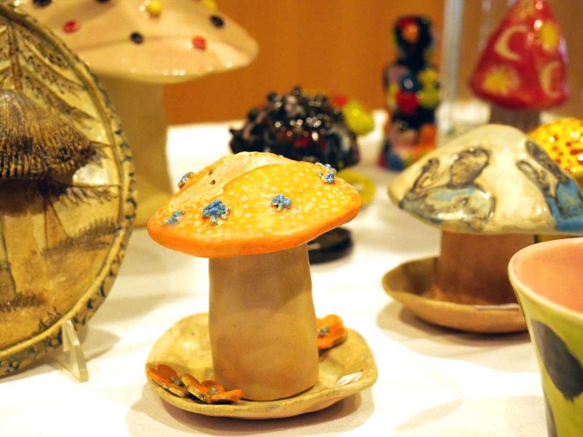 Photograph of ceramic sculptures arranged on a table including a yellow and orange clay mushroom with small blue spots.