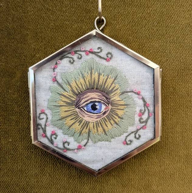 Handmade pendant depicting a vibrant blue eye surrounded by decorative embellishments.