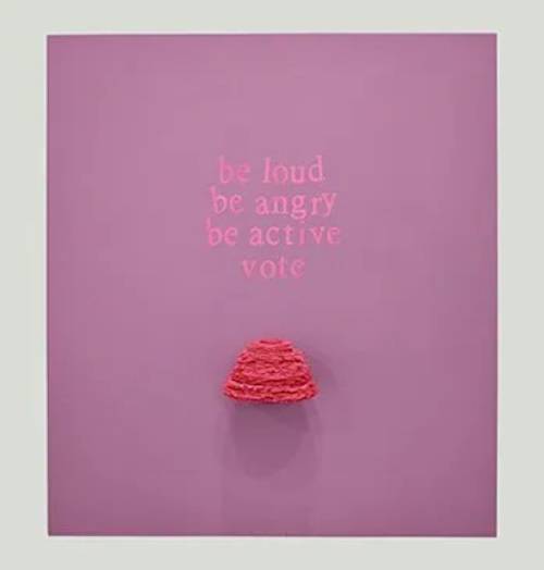 Space painting of a pink canvas with the words "be loud, be angry, be active, vote" above a red beanie hat.