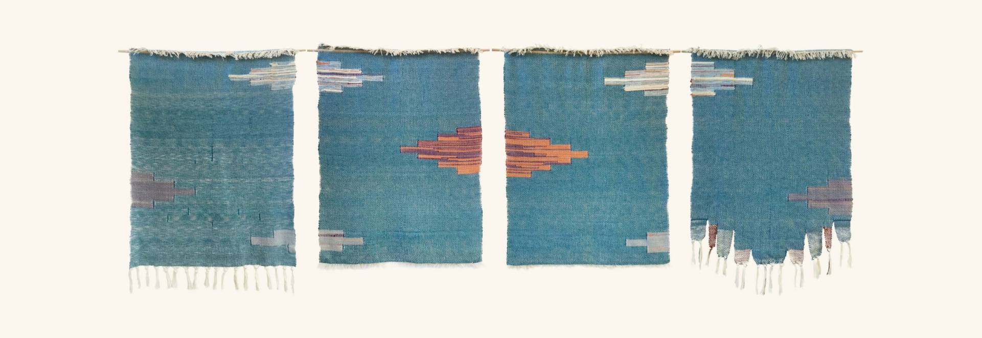 Photograph of a row of four wall hangings whose light blue hue and cloud-like patterns resemble an abstracted sky.