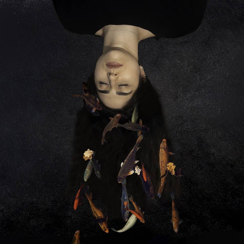 Digital photo montage of an Iranian woman, upside down and lying back, with colorful fish superimposed on her draped hair.