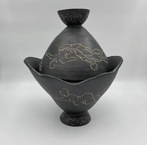 Photograph of a black ceramic vessel with etchings of drifting female figures.