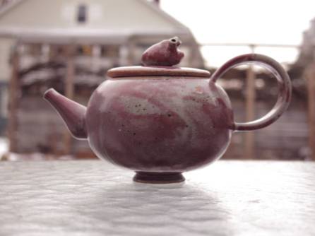 Handmade ceramic teapot sitting on an outdoor table.