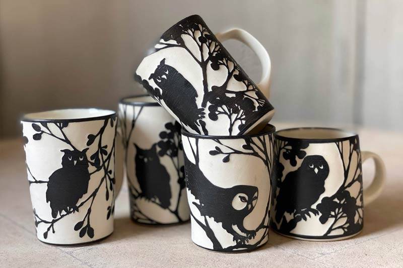 Photograph of five black and white handmade mugs depicting owls.